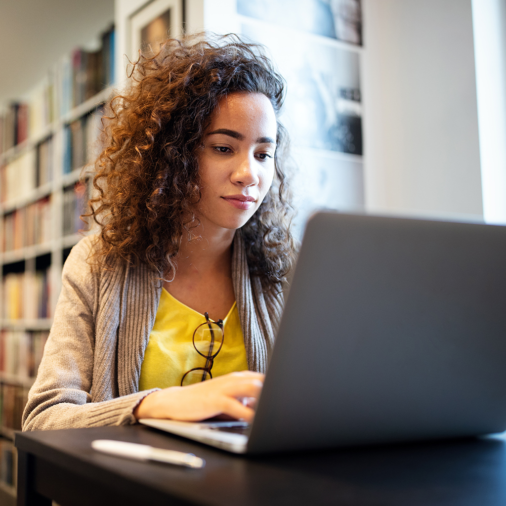 Young female student working om laptop in college library.